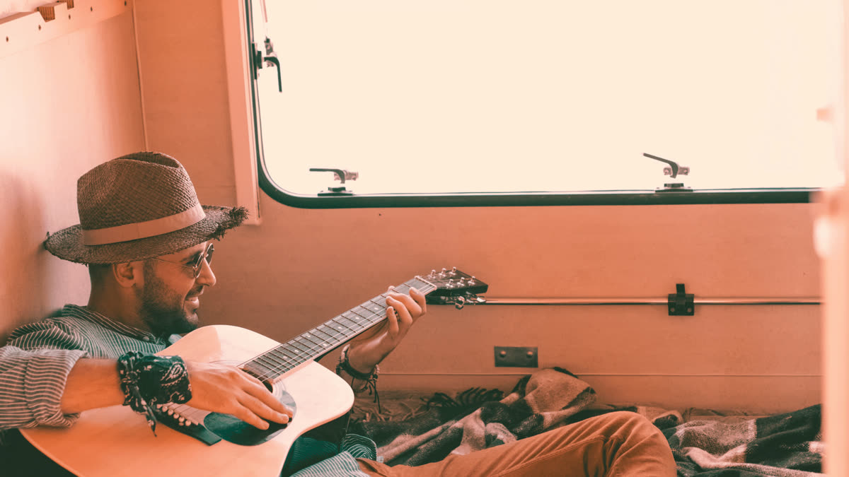 Künstler spielt Akustikgitarre, sitzend in einem Campervan im warmen Licht